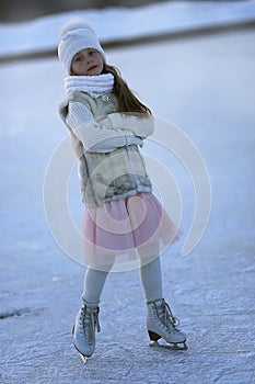 Adorable little girl in the white clothes and hat on the ice rink