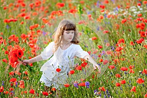 Adorable little girl in white dress playing in poppy flower field. Child picking red poppies. Toddler kid having fun in summer me