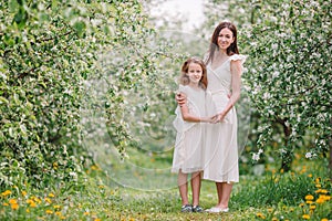 Adorable little girl with young mother in blooming cherry garden on beautiful spring day