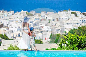 Adorable little girl and young mother in outdoor swimming pool background Mykonos town on Cyclades, Greece
