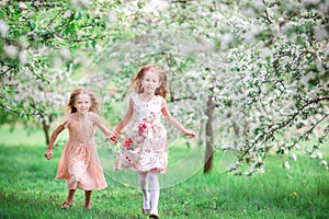 Adorable little girls in blooming cherry tree garden on spring day