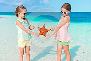 Adorable little girls having fun on the beach full of starfish on the sand