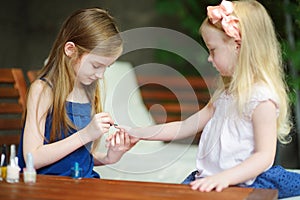 Adorable little girls having fun playing at home with colorful nail polish doing manicure and painting nails