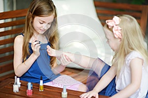 Adorable little girls having fun playing at home with colorful nail polish doing manicure and painting nails