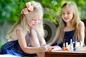 Adorable little girls having fun playing at home with colorful nail polish doing manicure and painting nails