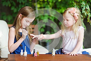Adorable little girls having fun playing at home with colorful nail polish doing manicure and painting nails