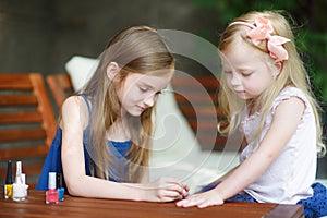Adorable little girls having fun playing at home with colorful nail polish doing manicure and painting nails