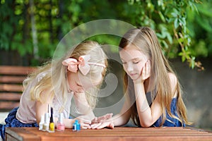 Adorable little girls having fun playing at home with colorful nail polish doing manicure and painting nails