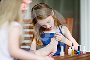 Adorable little girls having fun playing at home with colorful nail polish doing manicure and painting nails