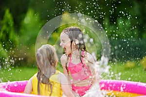 Adorable little girls playing in inflatable baby pool. Happy kids splashing in colorful garden play center on hot summer day.
