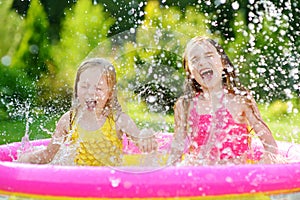 Adorable little girls playing in inflatable baby pool. Happy kids splashing in colorful garden play center on hot summer day.