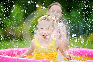 Adorable little girls playing in inflatable baby pool. Happy kids splashing in colorful garden play center on hot summer day.