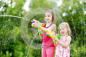 Adorable little girls playing with water guns on hot summer day. Cute children having fun with water outdoors.