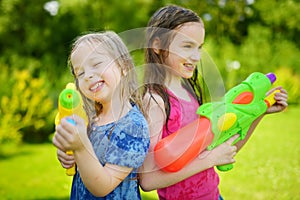 Adorable little girls playing with water guns on hot summer day. Cute children having fun with water outdoors.