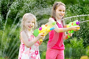 Adorable little girls playing with water guns on hot summer day. Cute children having fun with water outdoors.