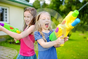 Adorable little girls playing with water guns on hot summer day. Cute children having fun with water outdoors.