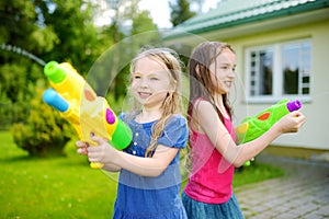 Adorable little girls playing with water guns on hot summer day. Cute children having fun with water outdoors.