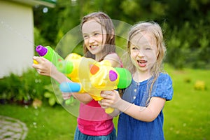 Adorable little girls playing with water guns on hot summer day. Cute children having fun with water outdoors.