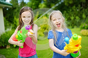 Adorable little girls playing with water guns on hot summer day. Cute children having fun with water outdoors.