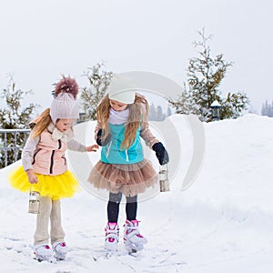 Adorable little girls skating on ice rink outdoors