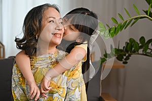 Adorable little grandchild hugging and kissing on cheek her grandmother. Family and love concept