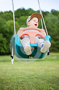 Adorable little happy Caucasian infant baby boy child swinging on playground outdoors.