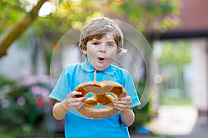 Adorable little kid boy eating huge big bavarian german pretzel.