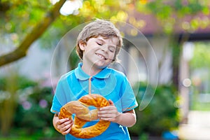 Adorable little kid boy eating huge big bavarian german pretzel.