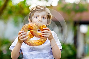 Adorable little kid boy eating huge big bavarian german pretzel.