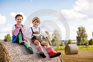 Adorable little kid boy and girl in traditional Bavarian costumes in wheat field on hay stack