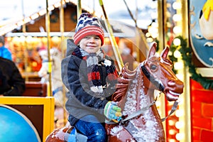 Adorable little kid boy riding on a carousel horse at Christmas funfair or market, outdoors.