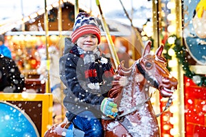 Adorable little kid boy riding on a merry go round carousel horse at Christmas funfair or market, outdoors. Happy child