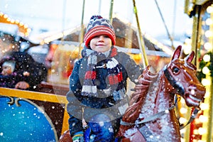 Adorable little kid boy riding on a merry go round carousel horse at Christmas funfair or market, outdoors. Happy child