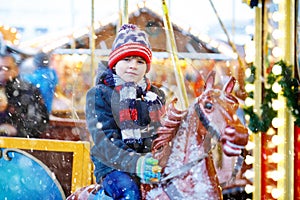 Adorable little kid boy riding on a merry go round carousel horse at Christmas funfair or market, outdoors. Happy child