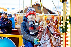 Adorable little kid boy riding on a merry go round carousel horse at Christmas funfair or market, outdoors. Happy child