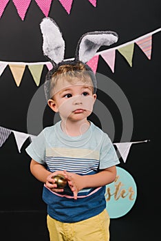 adorable little kid with bunny ears and golden easter egg in hands
