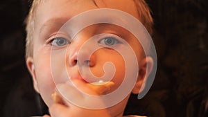 An adorable little kid is eating the waffle cup of white vanilla ice cream and looks into camera with his blue eyes in