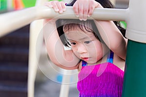 Adorable little kid girl in brightly colored dress is about to hang on to the bar. Children are afraid of sensational exercise.