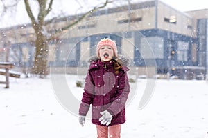 Adorable little kid girl in colorful clothes playing outdoors during snowfall