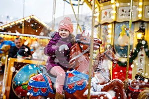 Adorable little kid girl riding on a carousel horse at Christmas funfair or market, outdoors.