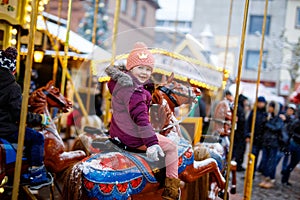 Adorable little kid girl riding on a carousel horse at Christmas funfair or market, outdoors.