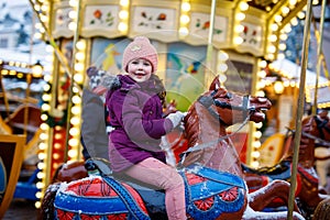 Adorable little kid girl riding on a carousel horse at Christmas funfair or market, outdoors.