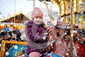 Adorable little kid girl riding on a carousel horse at Christmas funfair or market, outdoors.