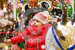 Adorable little kid girl riding on a merry go round carousel horse at Christmas funfair or market, outdoors. Happy