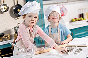 adorable little kids in chef hats and aprons smiling at camera while cooking together