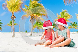 Adorable little kids have fun in Santa hat during Christmas beach vacation. New Year on the beach