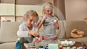 Adorable little kids painting colorful Easter eggs together, sitting on a couch while spending time at home