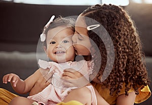 Adorable little mixed race child kissing baby sister on the cheek at home. Two small cute hispanic girls sitting