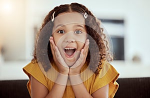 Adorable little mixed race child touching face with her hands in surprise at home. One small cute hispanic girl sitting