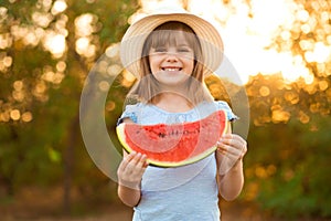 Adorable little preschool child girl with blond hairs and hat eating watermelon in summer holidays. Funny happy child